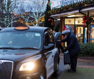 A clean Waltham Cross Taxis vehicle parked on a festive street in Waltham Cross during Christmas, with lights in the background.